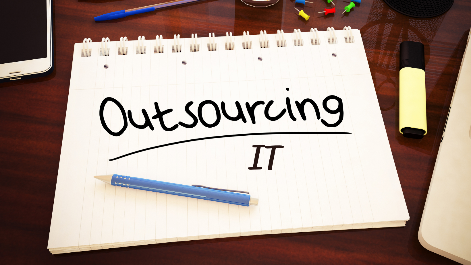 Notepad with writing on a page saying Outsourcing IT